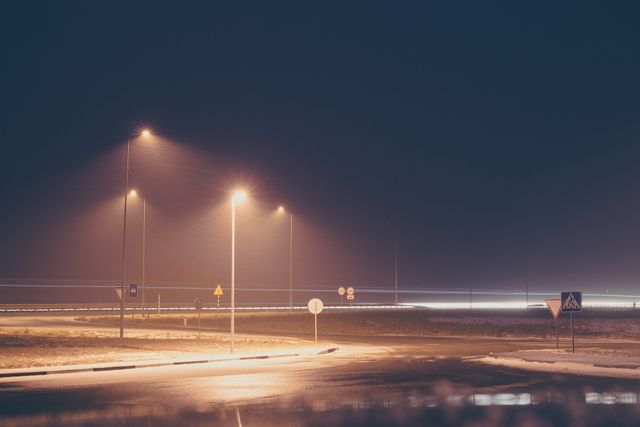 Street lights illuminating foggy road at night with car light trails creating a scene of motion and stillness. Ideal for use in themes related to urban life, transportation, and night time settings. Can be used in articles, blogs about night photography, city infrastructure, and road safety.
