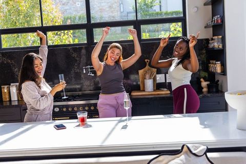 Sunlit kitchen dance party friends in loungewear and activewear celebrating with champagne