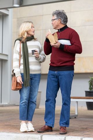 Senior couple chatting while enjoying takeout and coffee in urban plaza, casual denim