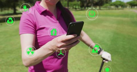 Golfer holding smartphone and club on fairway checking green energy and recycling icons