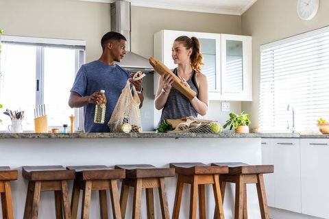 Couple unpacking groceries on kitchen island with baguette, herbs and olive oil