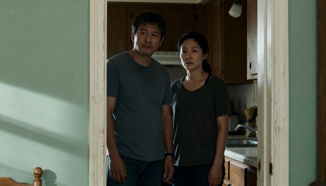 Worried asian couple standing in kitchen doorway wearing gray tees and casual jeans