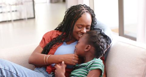 African american mother and daughter cuddling on sofa sharing warm laughing moment