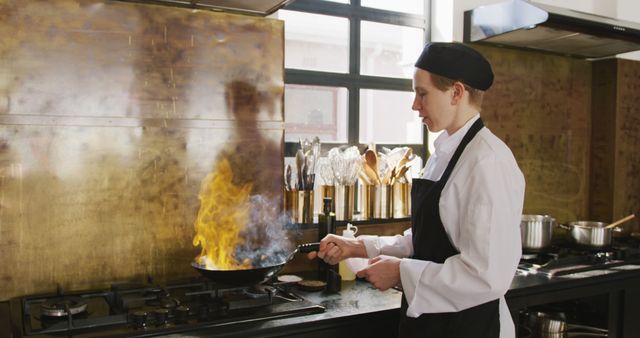 This image depicts a professional chef cooking with an open flame in a modern kitchen. The chef is wearing a white uniform, black apron, and a chef's hat. The image is ideal for use in culinary websites, restaurant promotions, cooking classes, food blogs, and advertisements for culinary schools. It showcases the dynamic and intense nature of professional cooking, highlighting skills and expertise in the kitchen.