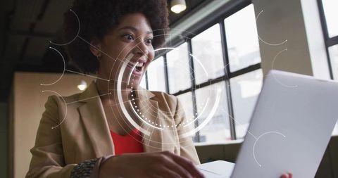 Smiling professional leaning toward laptop with futuristic hud overlay in modern coworking office