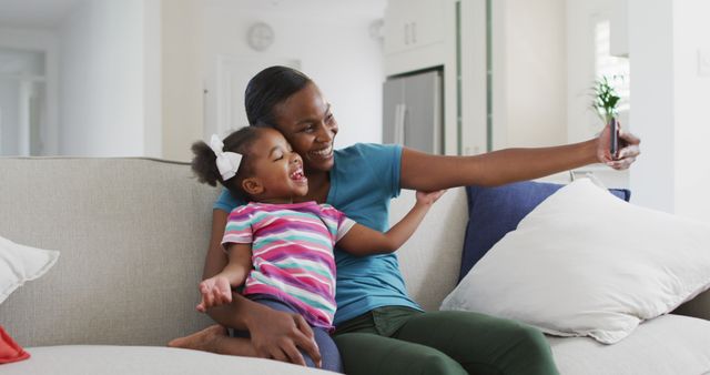 Happy african american mother and daughter sitting on sofa taking selfie at home - Download Free Stock Photos Pikwizard.com