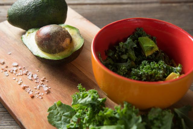 Fresh avocado and kale salad preparation on a wooden table. Ideal for use in articles or blogs about healthy eating, vegan recipes, organic food, and nutritious meal preparation. Perfect for promoting kitchenware, cooking classes, or food-related products.