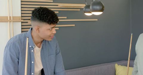 Young African American man playing pool in modern lounge with stylish pendant lighting and sofa