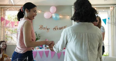Smiling woman passing gift at baby shower with pink balloons, banner, cupcakes