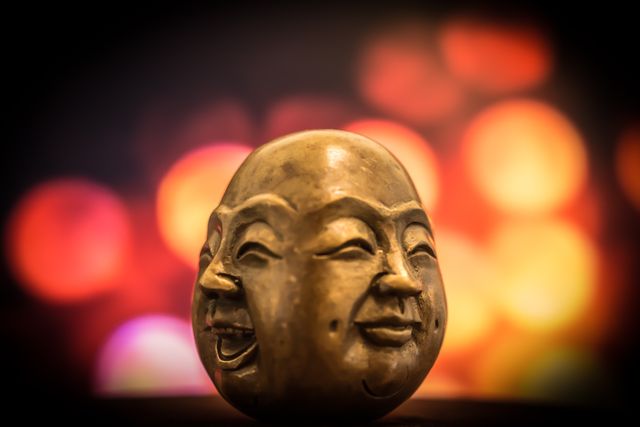 This image features a close-up view of a Buddha statue displaying a smiling face, with a colorful bokeh background. The serene expression of the statue adds a sense of calm and positivity. Ideal for use in projects related to spirituality, meditation, art, or cultural studies. Suitable for websites, blogs, advertising, and printed materials focused on zen practices and peaceful living.