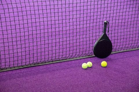 Black padel racket leaning against net on vibrant purple court with fluorescent balls