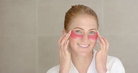 Woman relaxing with red under-eye gel patches in bathroom