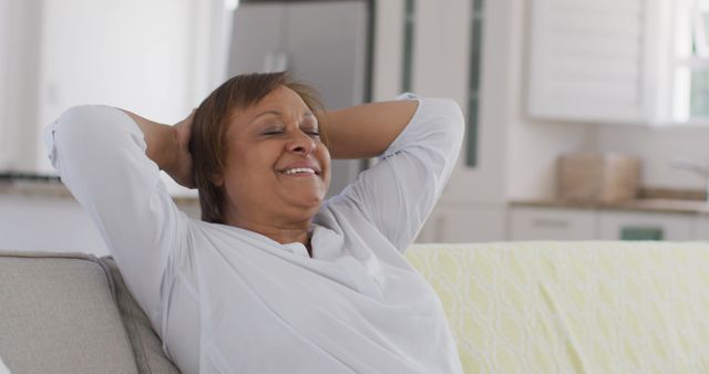 Smiling woman relaxing with arms behind head on a couch at home. Perfect for concepts of leisure, home comfort, mental well-being, peaceful afternoon routines, and showcasing relaxed lifestyle moments.