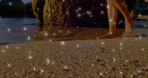 Male walking barefoot on pebble beach at golden hour with sparkling sand and tidal pool