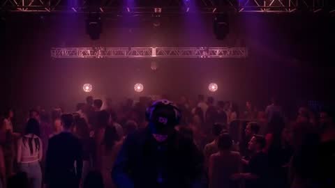 DJ Cueing Tracks and Adjusting Mixer as Crowd Grows Under Purple Club Lights