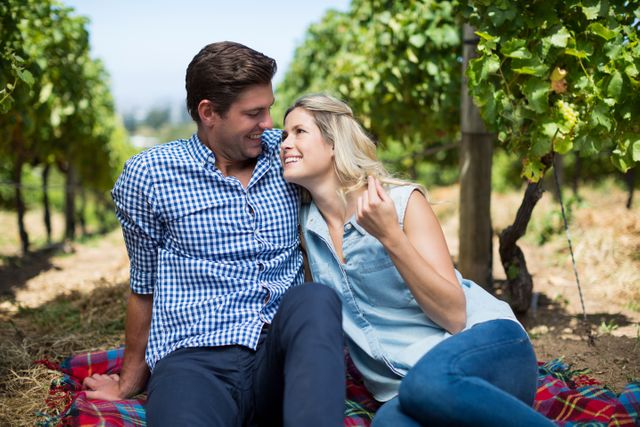 Happy young looking at each other while sitting together at vineyard