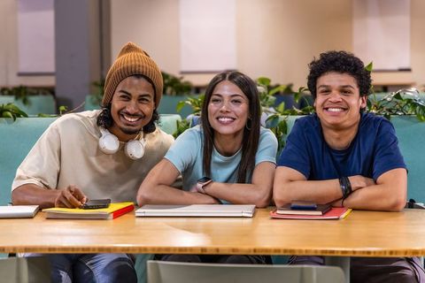 Smiling multicultural students studying together in modern campus lounge with laptops