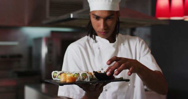Biracial male chef standing in kitchen making a nice plate of sushi. business colleagues working together.