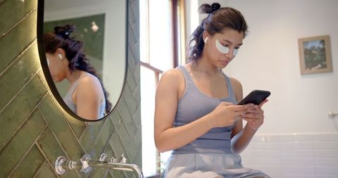 Teen Girl Practicing Self-Care While Using Smartphone in Modern Bathroom
