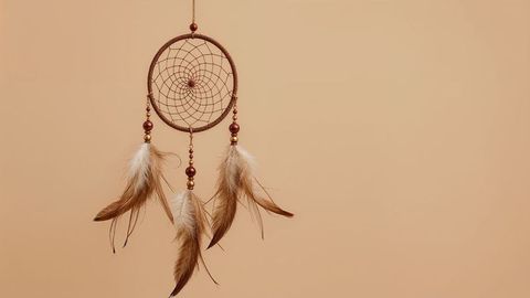 Hanging dreamcatcher with feathers and beads against neutral background