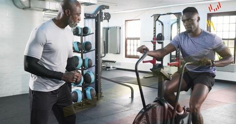 Young athlete pedaling air bike while coach guiding high-intensity cardio session