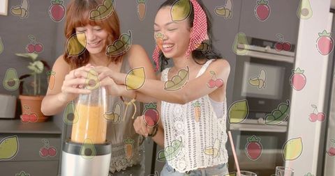 Two women blending orange smoothie in home kitchen laughing with playful fruit overlay