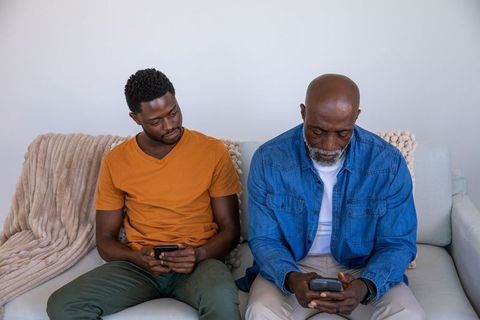 Father and Son Engaged in Smartphones While Sitting on Sofa