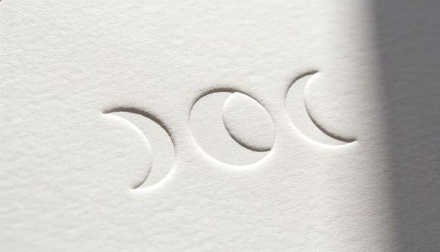 Depicting blind-embossed lunar cycle on textured paper with soft side lighting