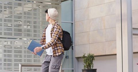 Young asian student standing at campus entrance holding blue notebook looking left