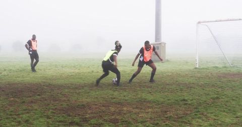 Athletes dribbling soccer ball in foggy field during practice match