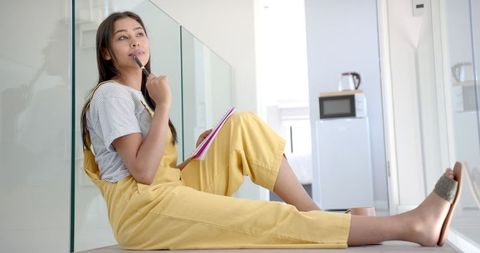 Young Woman Pondering at Home with Notebook
