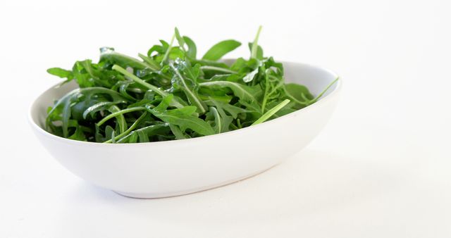 Fresh arugula in a white bowl against a clean white background, ideal for promoting healthy eating, diet plans, and organic foods. Perfect for use in recipes, cooking blogs, nutrition websites, and dietary posters.