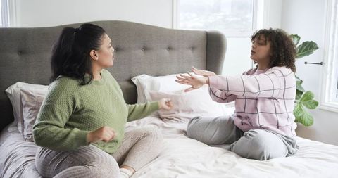 Multiracial women sharing animated conversation while sitting on cozy bed in bedroom