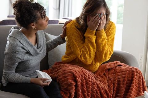 Multiracial friends comforting woman crying on couch with cozy blanket and tissues