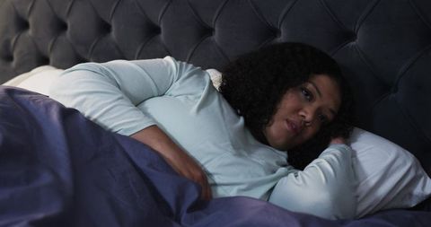 African American Woman Lying in Bed, Contemplative, Tufted Headboard and Navy Duvet