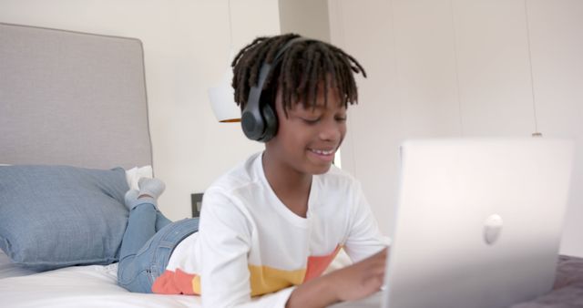 Smiling African American Boy Using Laptop with Headphones on Bed - Download Free Stock Images Pikwizard.com