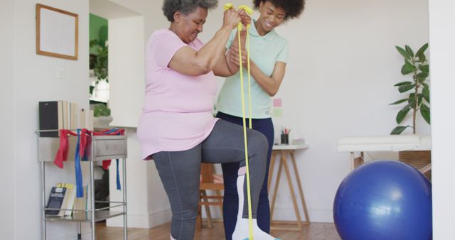 Elderly woman receiving assistance from a therapist during a physical therapy session. Ideal for use in articles or websites focused on senior health, physical therapy programs, rehabilitation activities, and promoting active lifestyles for the elderly.