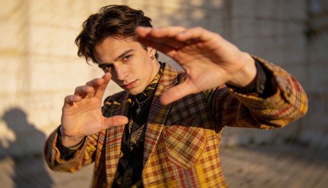 Young man reaching forward wearing plaid blazer and leaf-print shirt, jewelry close-up