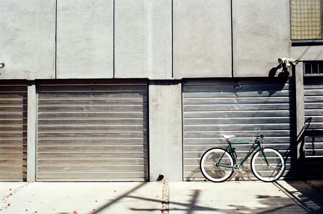 Bicycle leaning against garage doors in an urban area with strong industrial vibes. Ideal for conveying themes of independence, solitude, and urban lifestyles. Perfect for use in marketing campaigns related to urban living, casual transport, or modern minimalist design concepts.
