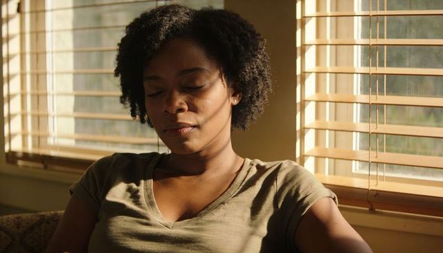 Relaxing woman basking in golden sunlight through wooden blinds on cozy sofa at home