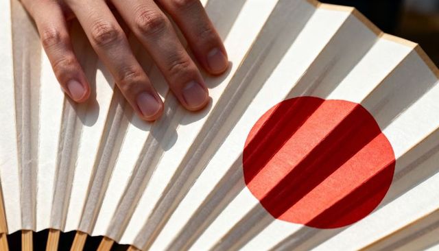 Adult hand touching japanese folding fan featuring red sun motif close-up texture study