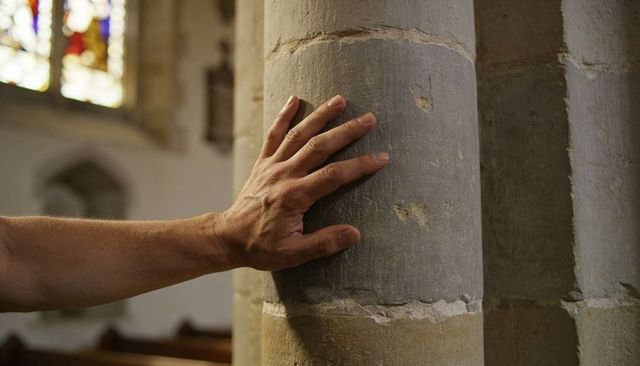 Pressing hand on weathered stone column under stained glass light in quiet chapel