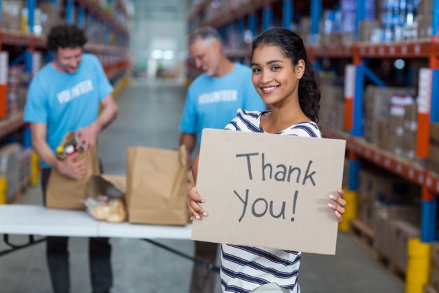 Portrait of woman holding sign boards with thank you message in warehouse