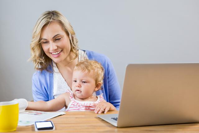 Mother holding baby girl while using laptop at home