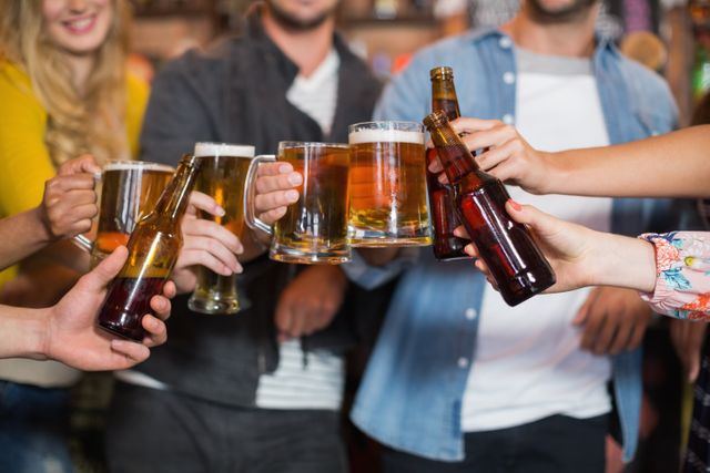 Group of friends raising beer glasses and bottles in a pub, celebrating and enjoying a night out. Perfect for use in advertisements for bars, pubs, and social events, as well as articles about nightlife, friendship, and celebrations.