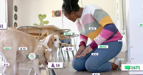Woman feeding two beagles in sunlit kitchen wearing colorful sweater with social overlay