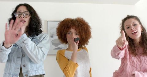 Diverse friends singing karaoke at home with handheld microphone and playful energy