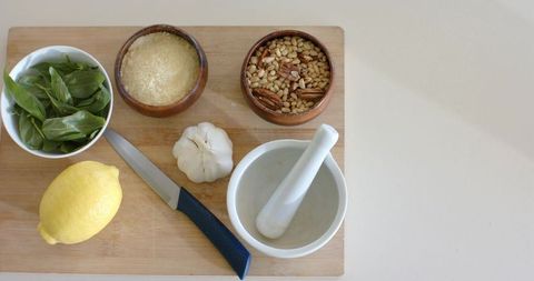 Pesto ingredients on wooden cutting board with mortar pestle knife lemon garlic basil