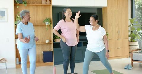 Senior african american women exercising at home doing yoga stretching and high-fiving