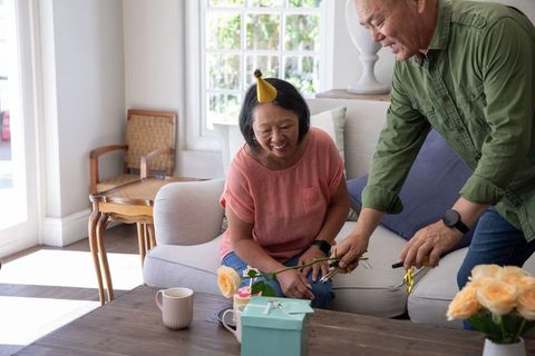 Chinese senior couple celebrating birthday, arranging roses and gifts in sunlit living room